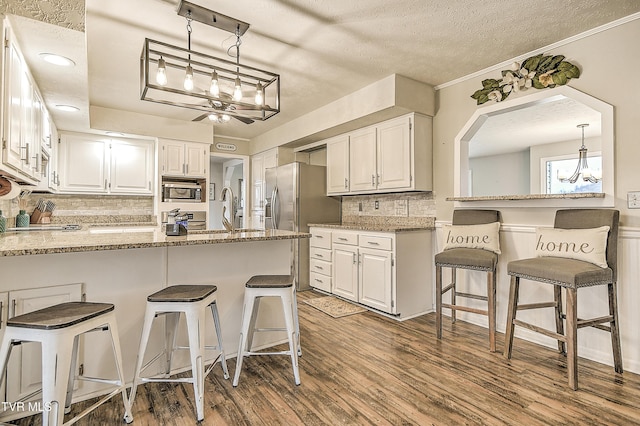 kitchen with white cabinets, appliances with stainless steel finishes, wood finished floors, a peninsula, and a sink