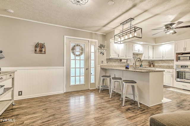 kitchen with a wainscoted wall, stainless steel appliances, wood finished floors, and white cabinetry