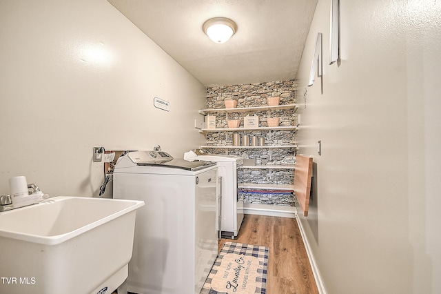 clothes washing area featuring light wood finished floors, washing machine and clothes dryer, a sink, laundry area, and baseboards