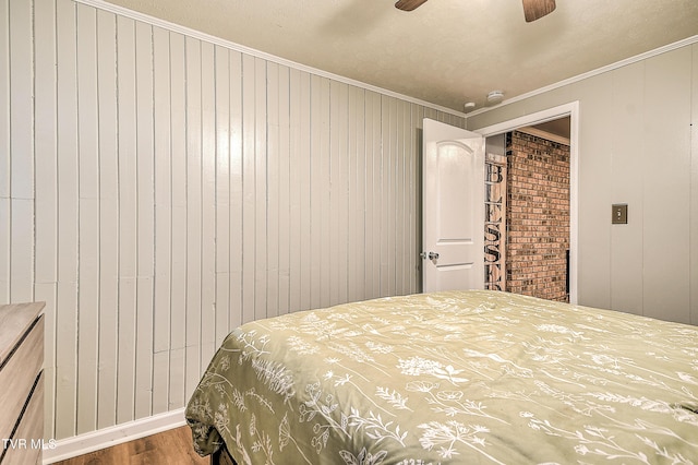 bedroom featuring a ceiling fan, wooden walls, ornamental molding, and wood finished floors