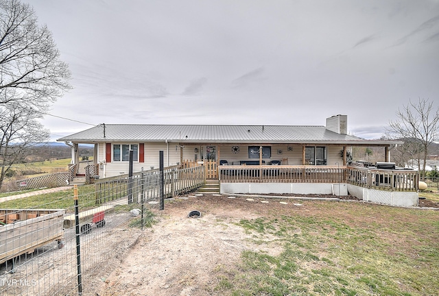 view of front facade featuring a chimney, a front yard, metal roof, a deck, and fence