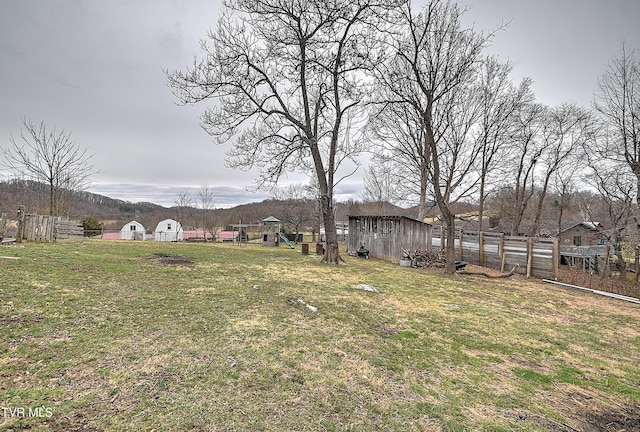 view of yard featuring an outbuilding, a playground, and fence