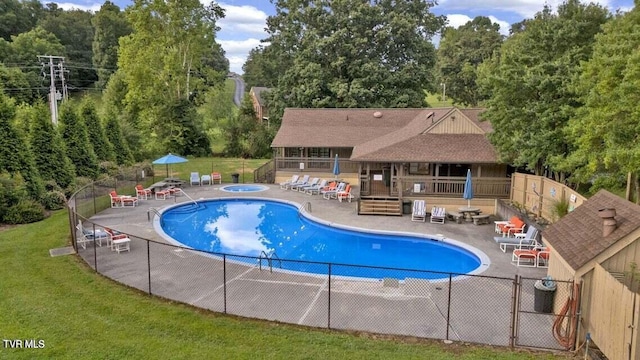 pool with fence, a community hot tub, a lawn, and a patio