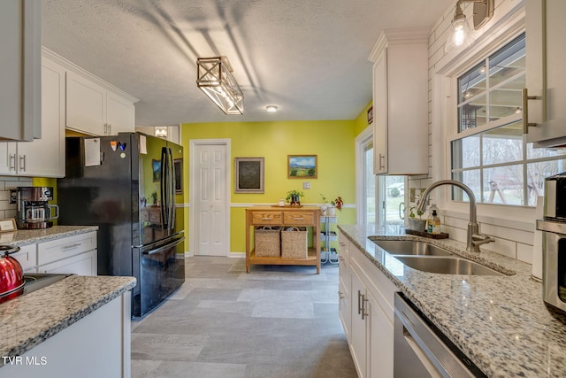 kitchen featuring white cabinets, freestanding refrigerator, a sink, light stone countertops, and stainless steel dishwasher