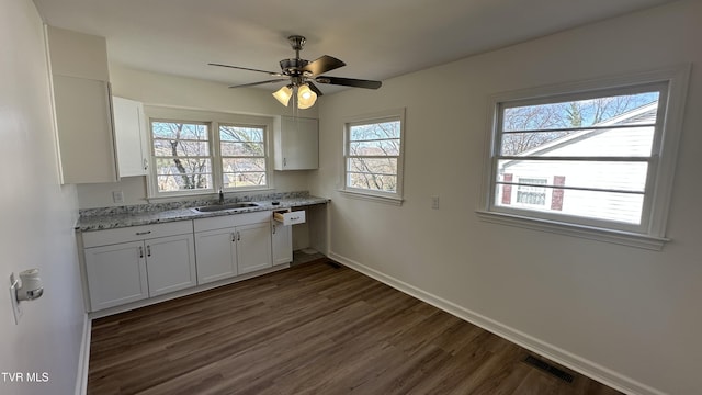 kitchen featuring dark wood-style flooring, a sink, visible vents, baseboards, and light stone countertops