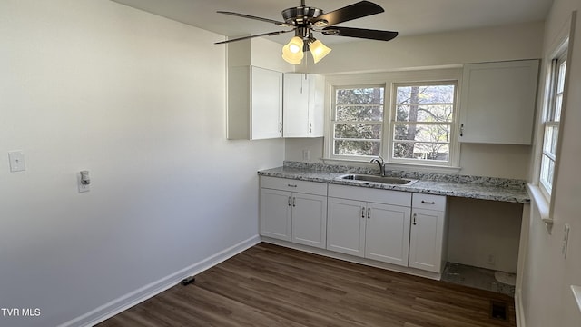 kitchen with light stone counters, dark wood-style flooring, a sink, white cabinetry, and baseboards