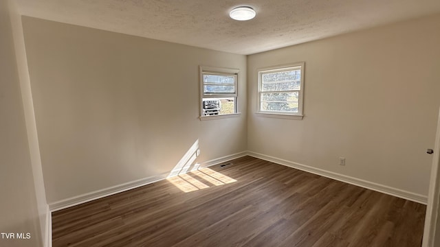 empty room featuring dark wood-style floors, visible vents, baseboards, and a textured ceiling