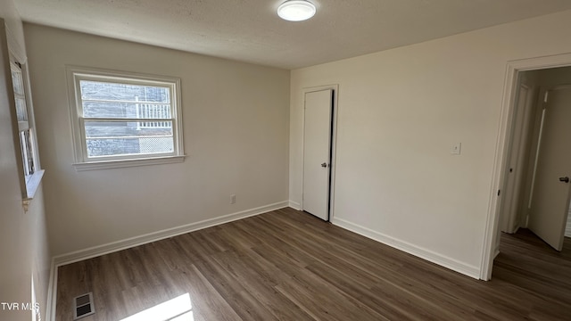 unfurnished bedroom with baseboards, visible vents, dark wood-type flooring, a textured ceiling, and a closet