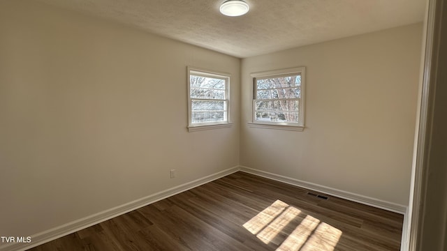 spare room with a textured ceiling, dark wood-style flooring, visible vents, and baseboards