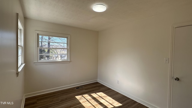 spare room featuring dark wood-type flooring, visible vents, a textured ceiling, and baseboards