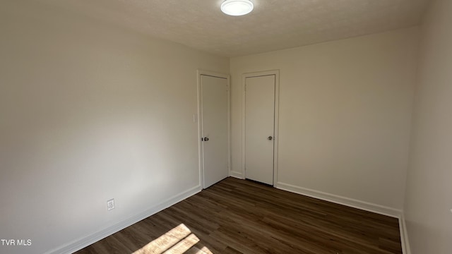 empty room with dark wood-style flooring, a textured ceiling, and baseboards