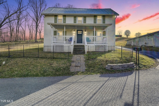 view of front of home with a yard, covered porch, metal roof, and a fenced front yard