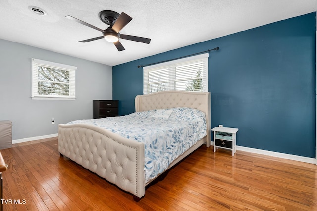 bedroom featuring hardwood / wood-style floors, multiple windows, baseboards, and a textured ceiling