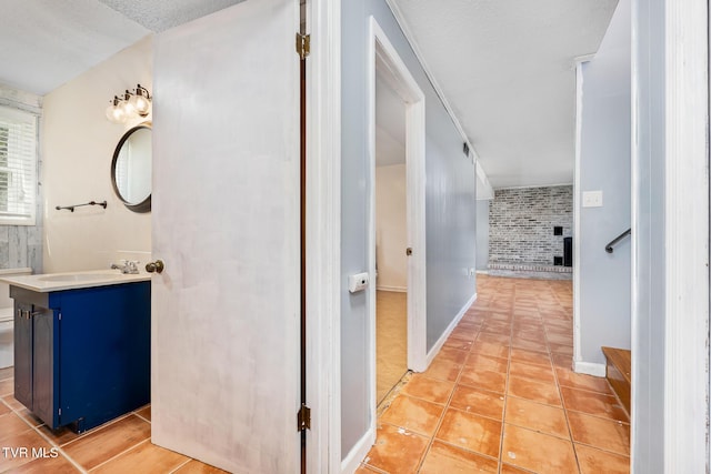 corridor with light tile patterned floors, baseboards, brick wall, and a sink