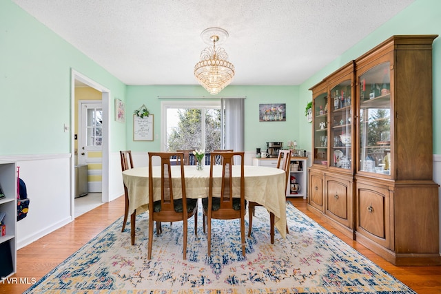 dining area featuring a notable chandelier, light wood-style floors, and a textured ceiling