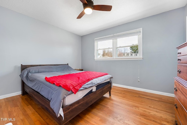 bedroom featuring light wood-type flooring, baseboards, a textured ceiling, and a ceiling fan