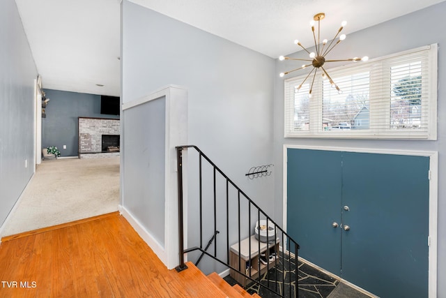 carpeted entryway featuring stairway, a fireplace, baseboards, and an inviting chandelier