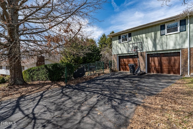 view of home's exterior featuring aphalt driveway, a garage, fence, and brick siding