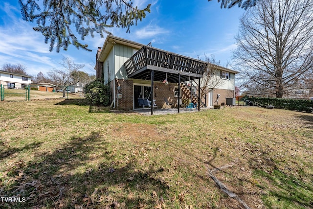 back of property with a lawn, a deck, fence, brick siding, and a patio area