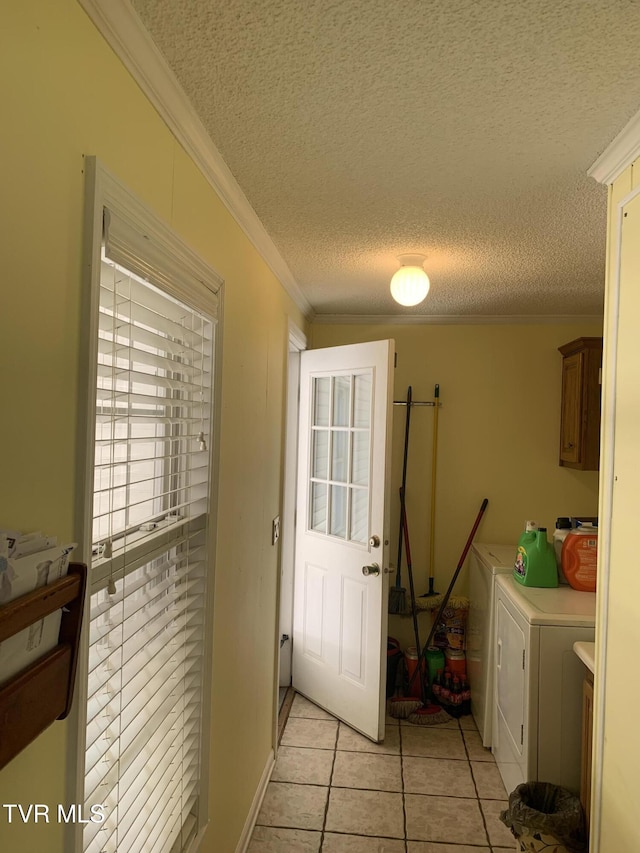 washroom with ornamental molding, a textured ceiling, cabinet space, light tile patterned floors, and washing machine and clothes dryer