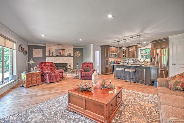 living area with a brick fireplace, light wood-style floors, a wealth of natural light, and ornamental molding