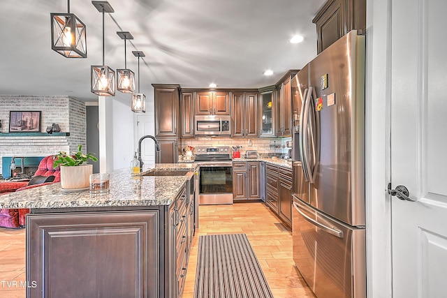 kitchen with light stone countertops, a sink, stainless steel appliances, light wood-type flooring, and backsplash