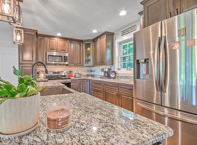 kitchen featuring glass insert cabinets, recessed lighting, appliances with stainless steel finishes, decorative backsplash, and light stone countertops