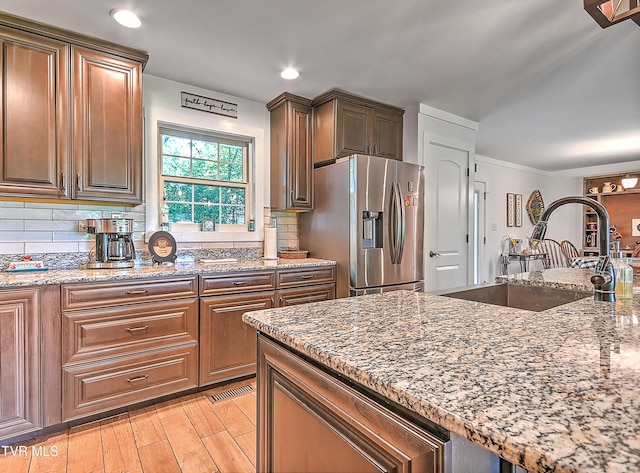 kitchen with light wood-type flooring, stainless steel refrigerator with ice dispenser, a sink, backsplash, and light stone countertops