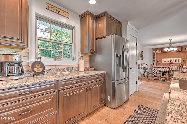 kitchen featuring a notable chandelier, stainless steel fridge, light wood finished floors, decorative backsplash, and light stone countertops