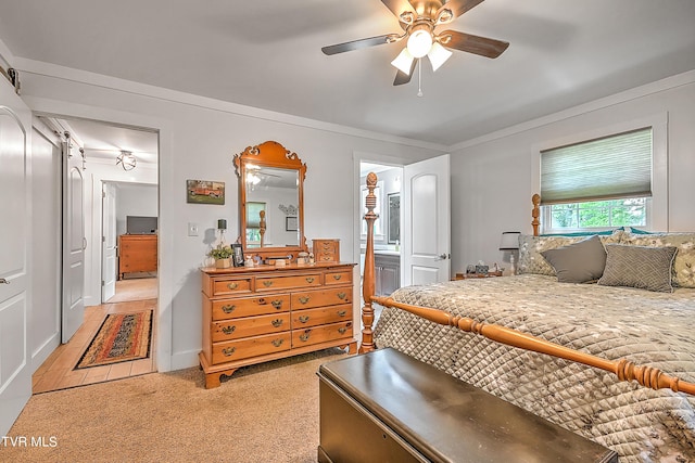 bedroom with a ceiling fan, crown molding, a barn door, light colored carpet, and connected bathroom