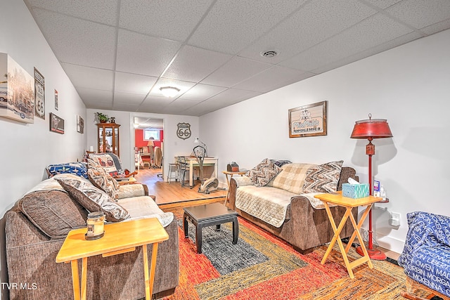 living area with a drop ceiling, visible vents, and wood finished floors