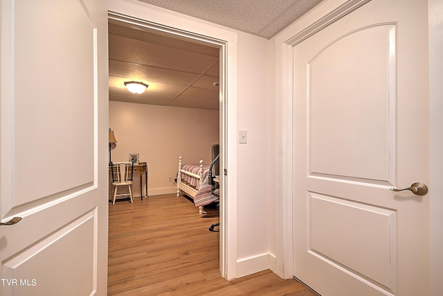 corridor featuring baseboards, a paneled ceiling, and light wood-style flooring