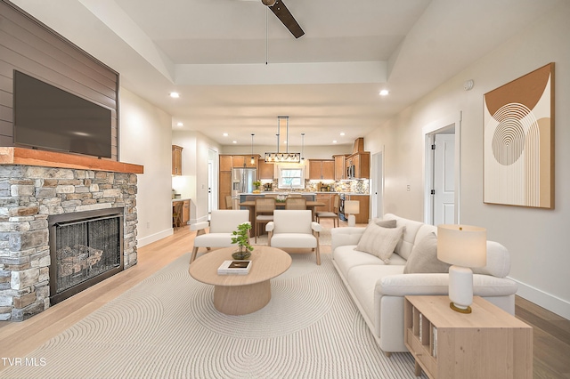 living room featuring recessed lighting, a tray ceiling, baseboards, and light wood-style floors