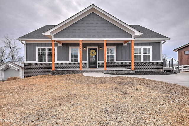 view of front of property with brick siding, board and batten siding, covered porch, and roof with shingles