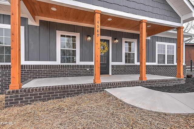 view of exterior entry featuring board and batten siding, brick siding, and covered porch