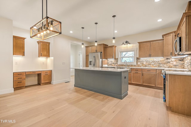 kitchen featuring tasteful backsplash, brown cabinetry, light wood-style floors, hanging light fixtures, and stainless steel appliances