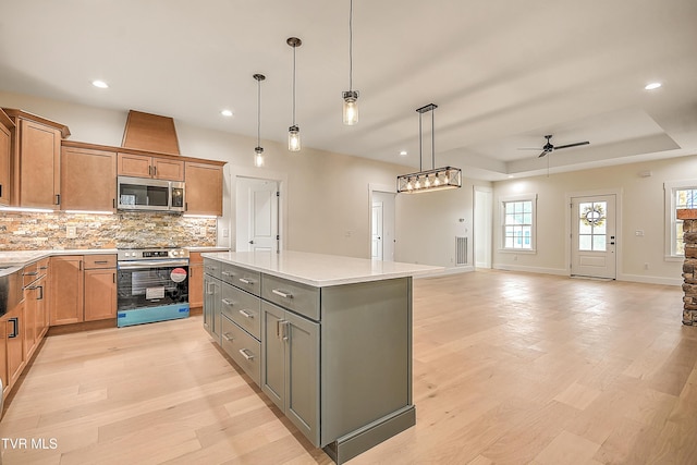 kitchen featuring light wood-style floors, a tray ceiling, backsplash, and appliances with stainless steel finishes