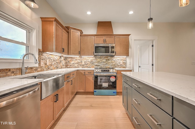 kitchen with light stone counters, decorative backsplash, light wood-style flooring, appliances with stainless steel finishes, and a sink