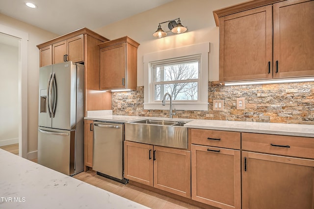 kitchen with a sink, backsplash, appliances with stainless steel finishes, and light wood finished floors