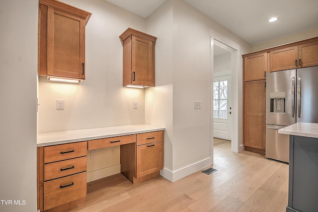 kitchen with light wood-style flooring, stainless steel refrigerator with ice dispenser, light countertops, baseboards, and built in study area