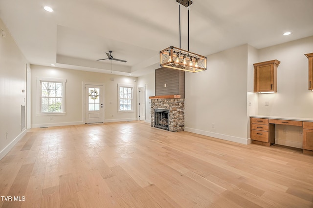 unfurnished living room featuring a raised ceiling, a fireplace, light wood finished floors, and built in study area