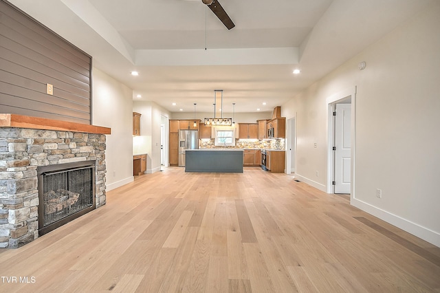 unfurnished living room featuring light wood-style flooring, a fireplace, a raised ceiling, and baseboards