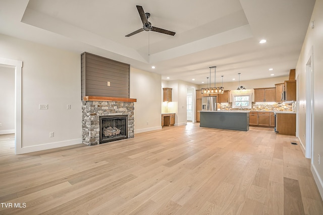 unfurnished living room with a raised ceiling, light wood-style floors, and a stone fireplace