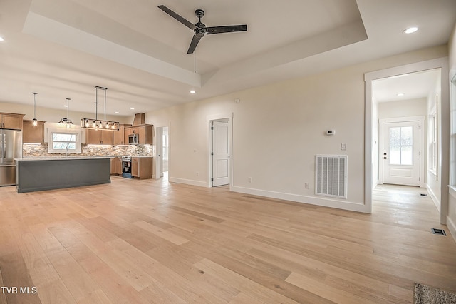 unfurnished living room featuring visible vents, a ceiling fan, light wood-style floors, and a tray ceiling