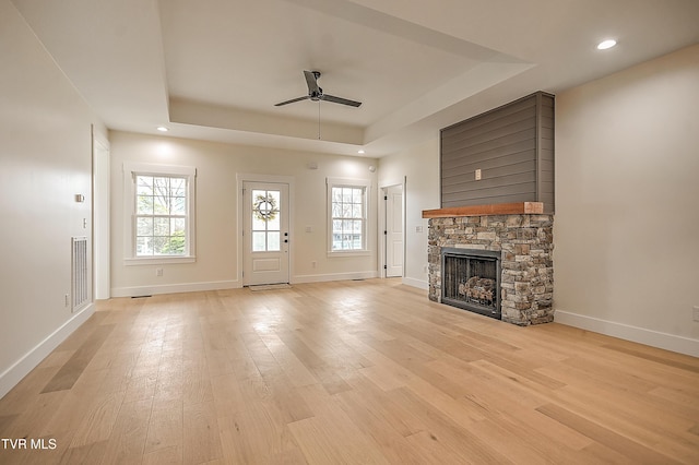 unfurnished living room featuring a ceiling fan, visible vents, baseboards, a raised ceiling, and light wood-type flooring