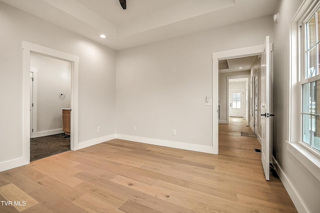 unfurnished room with a raised ceiling, recessed lighting, baseboards, and light wood finished floors