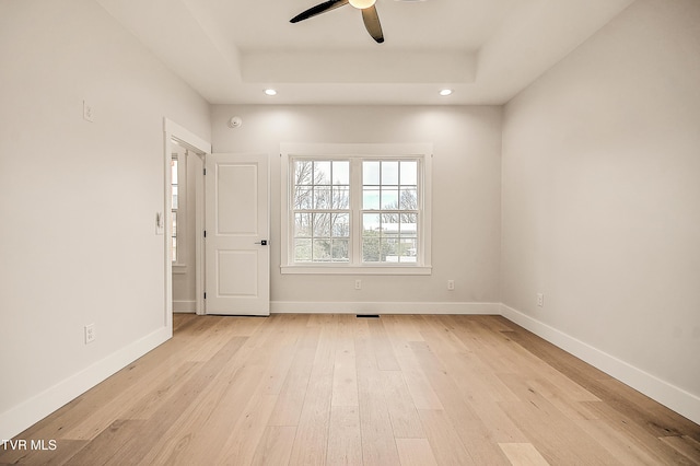 spare room with a raised ceiling, recessed lighting, baseboards, and light wood-type flooring