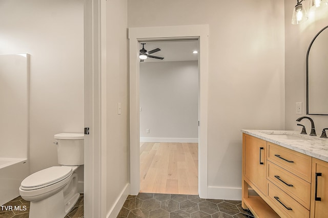 bathroom with toilet, a bathing tub, baseboards, ceiling fan, and vanity