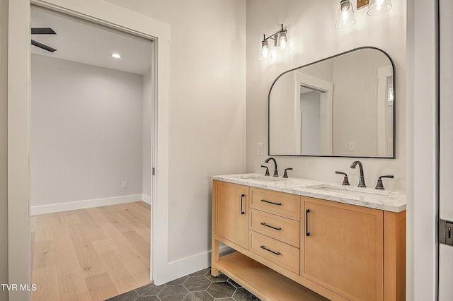 full bathroom featuring a sink, baseboards, wood finished floors, and double vanity