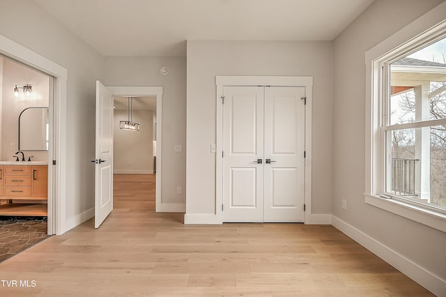 unfurnished bedroom featuring light wood-type flooring, baseboards, a closet, and ensuite bath